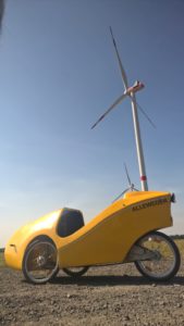 Velomobile in fron of a wind-turbine in blazing sun-light